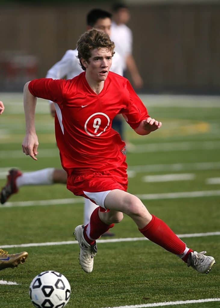 man in red soccer jersey running with ball